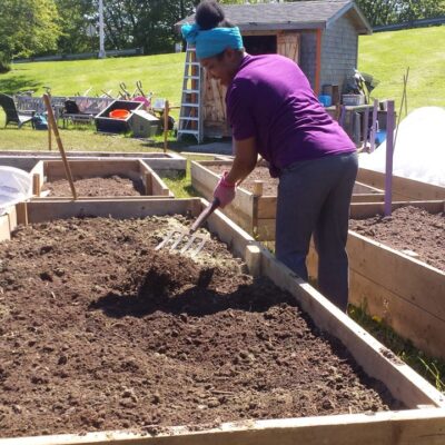 A smiling person prepares a raised plot for planting with a pitch fork.