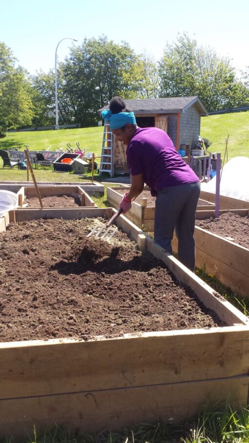 A smiling person prepares a raised plot for planting with a pitch fork.
