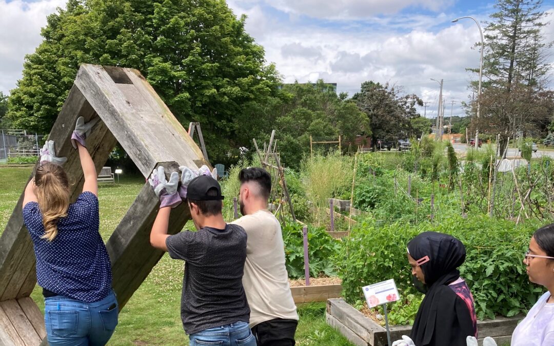 Three people push a garden box up on end, moving it across the farm. Two people look on